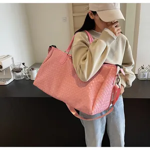 Woman carrying a large pink woven travel bag over her shoulder in a stylish cafe setting