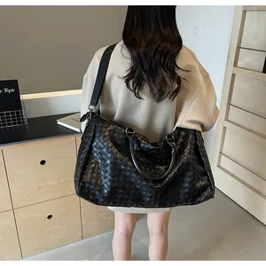 Large black woven travel duffel bag carried by a model, showing texture and size.
