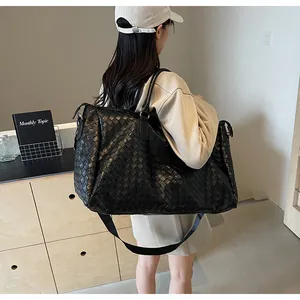 Large black woven travel bag for women worn by model in minimalist indoor setting