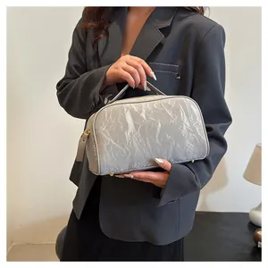 Detailed close-up of a stylish silver wrinkled texture cosmetic bag held by a model