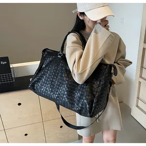Asian woman carrying a large black woven leather travel bag in a modern room setting