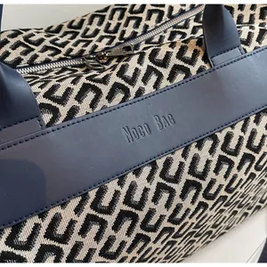 Détail de la garniture en cuir bleu avec logo embossé sur un sac de voyage en jacquard