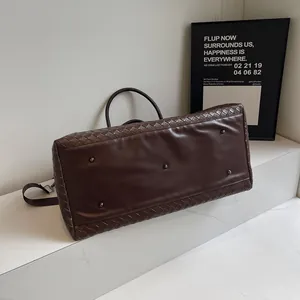 Detail view of the woven brown travel bag with metal feet on marble surface.