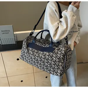 Gros plan d'un sac de voyage monogramme bleu marine et crème porté à l'épaule par un mannequin.