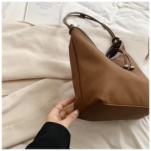 Detailed view of a large brown minimalist tote bag with thin leather shoulder straps.