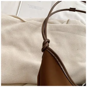 Detailed view of the brown leather tote bag's knotted strap and soft matte texture.