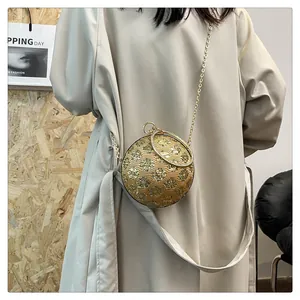 Detailaufnahme einer goldenen kugelförmigen Abendtasche mit floralem Muster am Model
