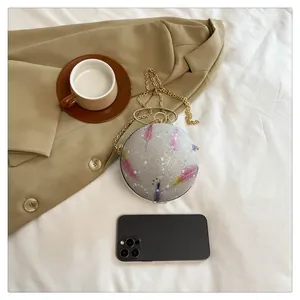 Detailansicht einer runden Abendtasche mit Federdruck neben einem Smartphone zum Vergleich