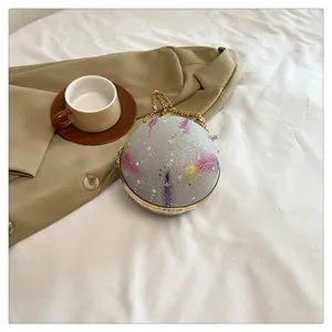 Nahaufnahme der glitzernden Kugel-Abendtasche mit Federprints und Goldkette.