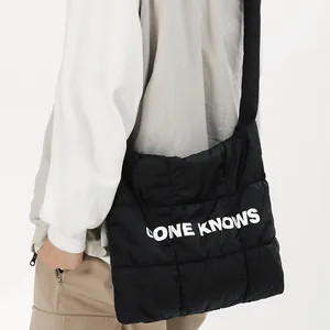 Vue latérale d'un sac cabas noir matelassé avec impression de lettres blanches porté à l'épaule