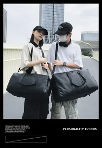 Vue latérale de deux modèles portant de grands sacs de voyage noirs tressés en ville