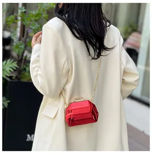 Elegante rode metalen mini-avondtas met gouden ketting over een witte blazer jas