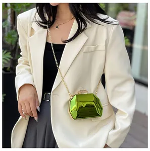 Detailopname van een groene metallic mini-avondtas met gouden ketting bij witte blazer