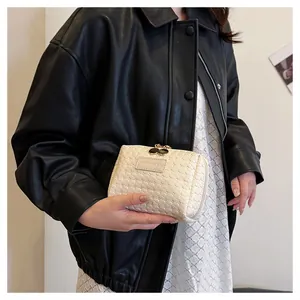 Elegant cream white woven grid cosmetic bag held by a model in a stylish black leather jacket