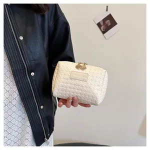 Detailed view of cream woven cosmetic bag held by a model in a leather jacket.