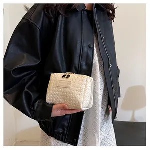 Detail view of a beige grid textured square cosmetic bag held in hand against a black jacket.