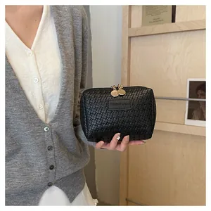 Detailed view of black woven texture on a stylish square cosmetic pouch with gold zippers.