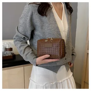 Close-up detail of a brown minimalist woven pattern square cosmetic bag held by a model