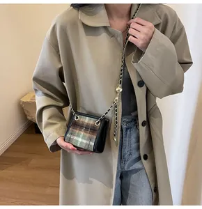 Detail shot of a plaid wool crossbody bag with a chain strap styled on a trench coat.