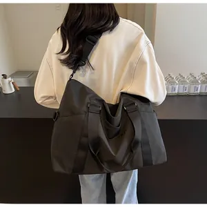 Rear view of a large black nylon travel bag worn by a model in a minimalist indoor setting.