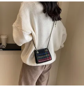 Detail view of a plaid woolen crossbody bag with a metal chain strap on a white sweater.