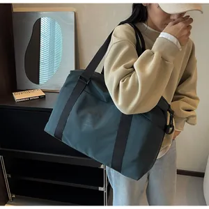Large dark green travel shoulder bag with trolley sleeve being worn by a female model