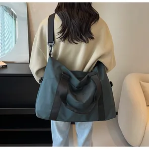 Detail view of model carrying a large dark teal travel bag in a modern interior setting