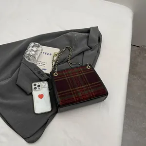 Detail view of a stylish plaid wool shoulder bag with a gold chain strap on a grey blazer