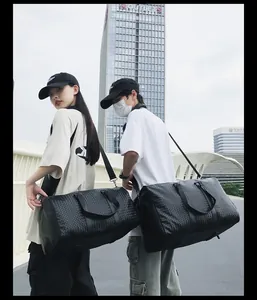 Modèles portant de grands sacs de voyage tissés noirs dans un cadre urbain extérieur.