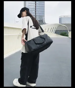 Mannequin portant un grand sac de voyage en cuir tissé noir sur un pont urbain.
