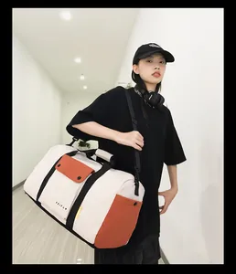 Grand sac de voyage crème et orange avec sangles noires porté par un mannequin dans un couloir