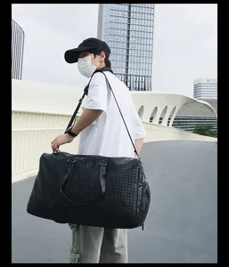 Sac de voyage noir en cuir tressé avec compartiment à chaussures porté par un mannequin.