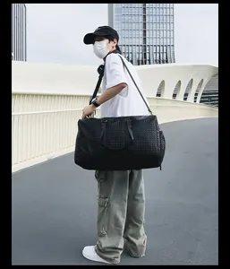 Détail du grand sac de voyage tissé noir porté par un mannequin en milieu urbain