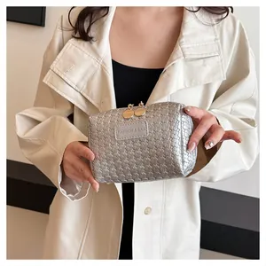 Close-up view of a stylish silver woven checkered makeup bag held by a person in a coat