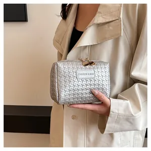 Close-up handheld view of a silver woven square cosmetic bag with gold zipper pulls.