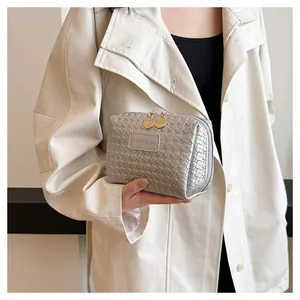 Detailed close-up of a silver woven lattice makeup bag with gold zippers held by a model