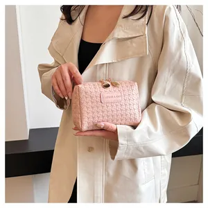 Close-up of a stylish pink woven checkered makeup bag held by a fashion model.