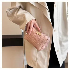 Close-up of a pink woven makeup bag held by a hand in a beige coat