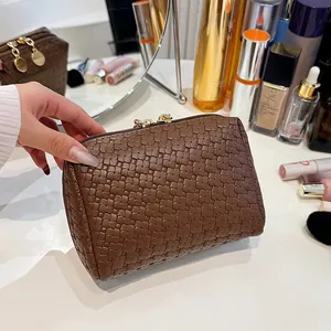 Close-up of a brown woven checkered makeup bag held against a vanity background