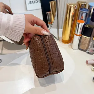 Detailed view of a brown crocodile pattern cosmetic bag held in hand to show texture and size