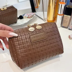 Macro view of a stylish brown woven square makeup bag with elegant gold zippers on a vanity.