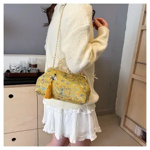 Close-up detail of yellow embroidered evening clutch with tassel and gold chain strap.