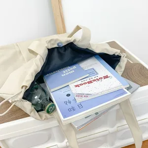 Grote beige nylon draagtas met trekkoordsluiting, gevuld met boeken en een fles