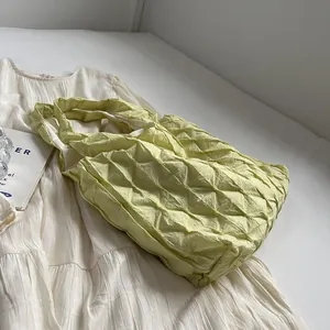 Detailed view of stylish lime green pleated grid tote bag on white textured summer dress