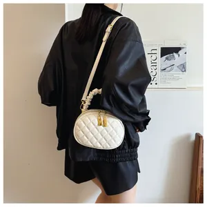 Detail of white quilted handbag with stylish ruffled handle and gold zippers.