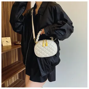 Detail view of white quilted oval handbag with ruffled handle and gold zippers