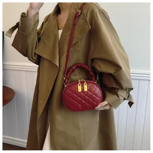 Red quilted oval crossbody bag with ruffled handle shown on model in trench coat