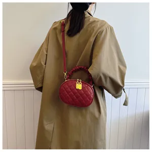 Red quilted crossbody bag with gathered handle worn by a model in a trench coat.