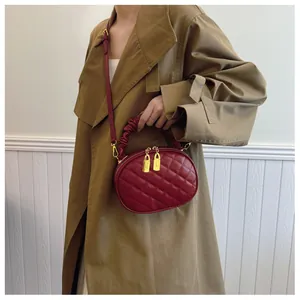 Red quilted oval crossbody bag with ruffled handle shown on model's beige trench coat