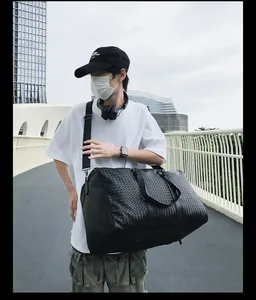 Photo lifestyle d'une personne portant un grand sac de voyage noir en cuir tressé